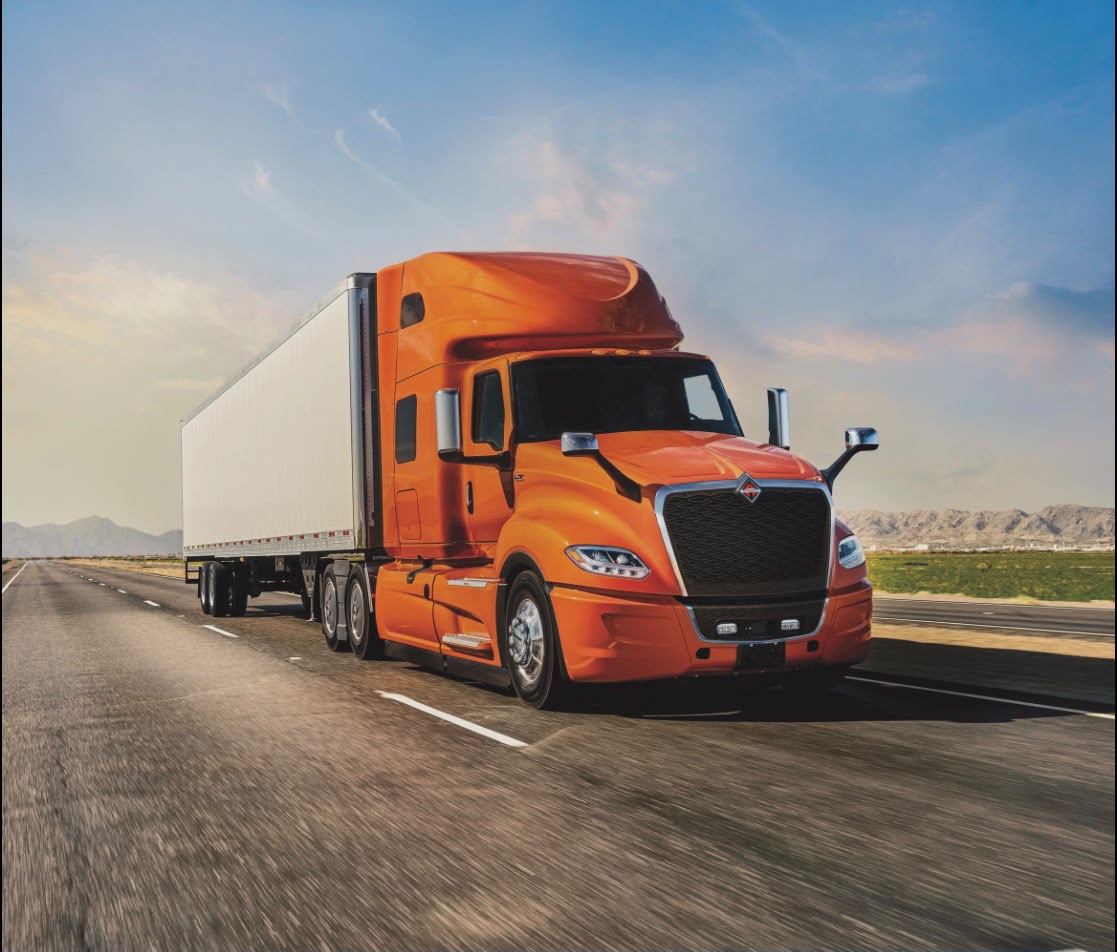 Semi truck driving along an open highway at sunset